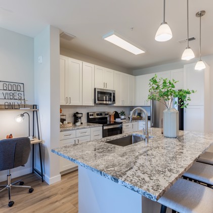 Modern open-concept kitchen featuring a granite island with stools in the foreground and white cabinets in the background